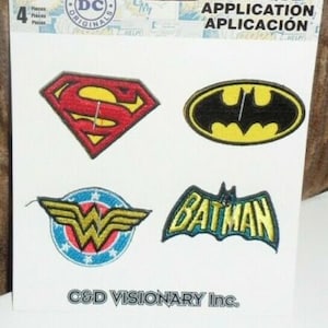 May include: A package of four DC Comics iron-on patches. The patches feature the Superman logo, the Batman symbol, the Wonder Woman emblem, and a Batman logo. The patches are in red, yellow, black, blue, and white.