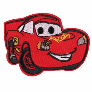 May include: Embroidered patch featuring a red cartoon race car with black tires and a smiling face. The car has white windshields, black eyes, and yellow and gold accents. The patch is designed to be ironed on.