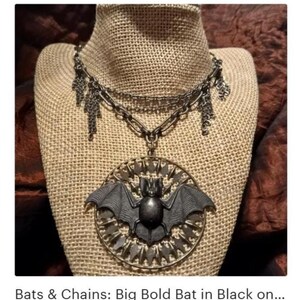 Puede incluir: Collar de estilo g&oacute;tico con un gran colgante de murci&eacute;lago detallado. El murci&eacute;lago negro tiene las alas extendidas, dentro de un marco circular. El collar tiene m&uacute;ltiples cadenas y colgantes decorativos.