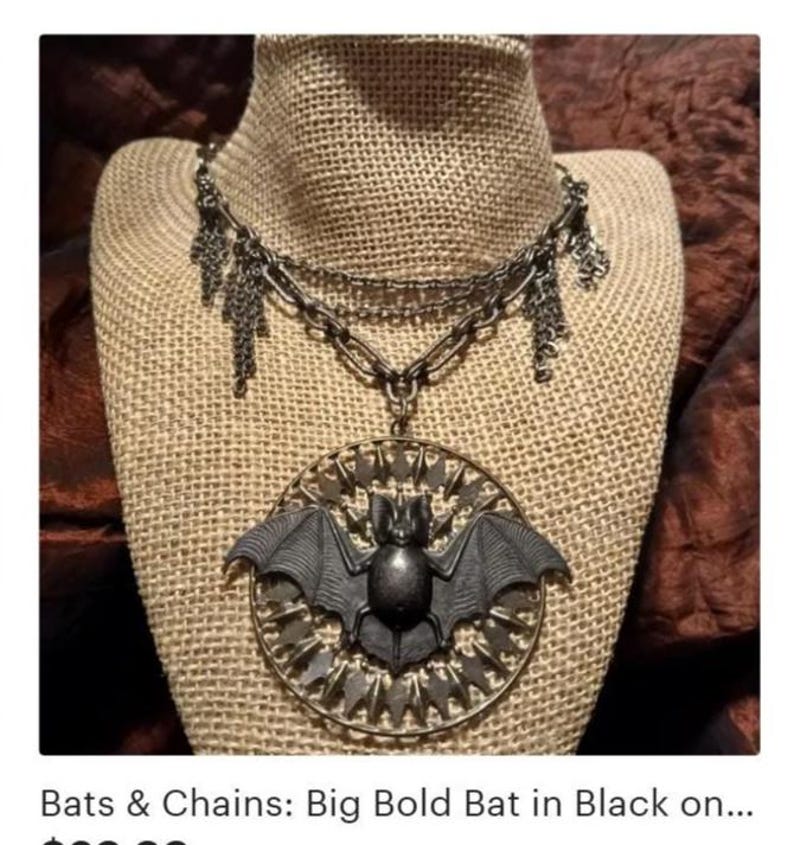 Puede incluir: Collar de estilo g&oacute;tico con un gran colgante de murci&eacute;lago detallado. El murci&eacute;lago negro tiene las alas extendidas, dentro de un marco circular. El collar tiene m&uacute;ltiples cadenas y colgantes decorativos.