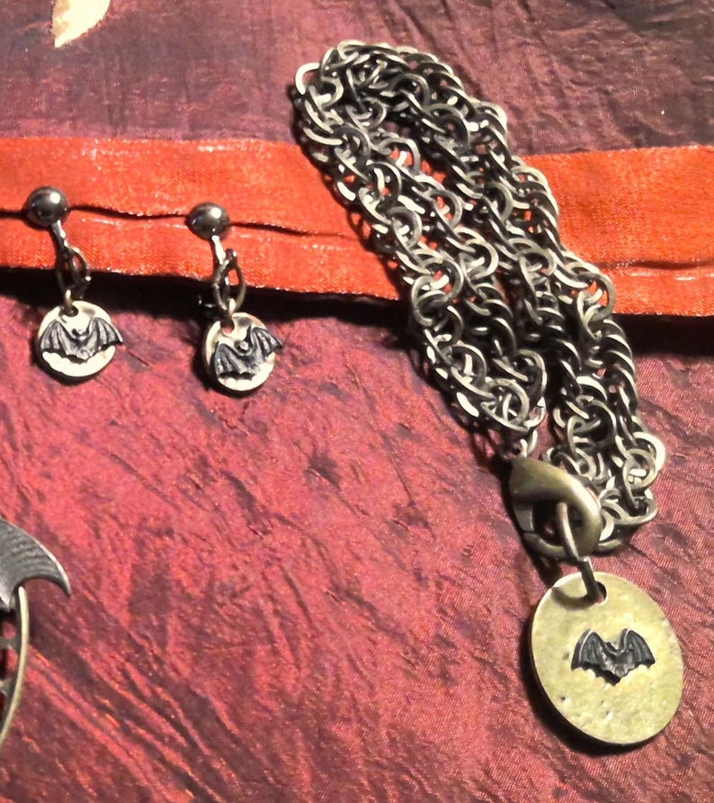 Puede incluir: Juego de joyas de estilo g&oacute;tico con motivo de murci&eacute;lago. El conjunto incluye un collar con cadena y colgante, y un par de pendientes. El colgante y los pendientes tienen un dise&ntilde;o circular con una silueta de murci&eacute;lago. La joyer&iacute;a es de metal.