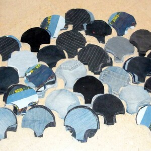 May include: A collection of fabric scraps in various shades of blue, black, and gray, cut into scallop shapes. The fabric scraps are arranged in a random pattern on a light brown surface.