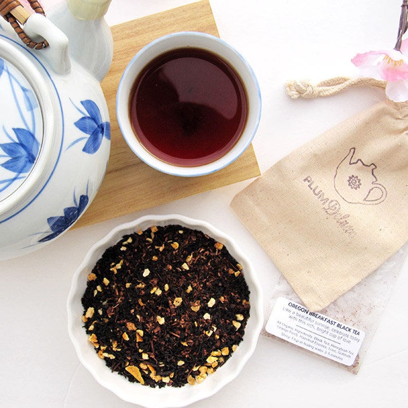 May include: An image of a tea set, including a floral teapot, a cup of tea, and a bowl of loose-leaf tea. A small bag with the text "PLUM Delave" and a tea bag with text are also present. The tea appears to be black tea.