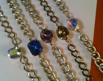 May include: Five silver and black chain bracelets with different colored gemstone accents. The gemstones are purple, blue, brown, and iridescent.