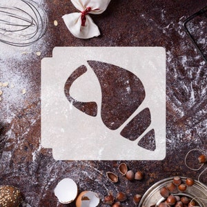May include: A white stencil with a crescent-shaped design on a brown surface covered in white flour. The stencil is for baking and creating a crescent-shaped design on baked goods.