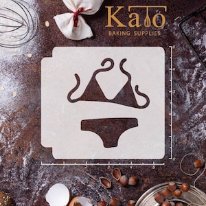 Puede incluir: Plantilla de plástico blanco de un bikini de arriba y abajo. La plantilla mide 12,7 cm de ancho y 12,7 cm de alto. La plantilla está sobre una superficie marrón con una regla y otros utensilios de repostería.