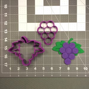 May include: Purple plastic cookie cutters shaped like a bunch of grapes, a single grape, and a grape leaf.