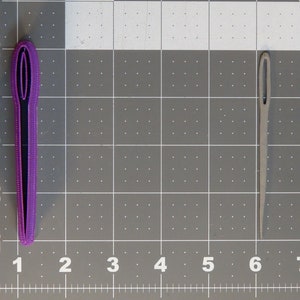 May include: Two needles, one purple and one grey, are shown against a grey grid background. The purple needle is larger than the grey needle.
