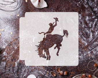 May include: A white stencil with a silhouette of a cowboy riding a bucking bronco. The stencil is on a brown surface with flour scattered around it.
