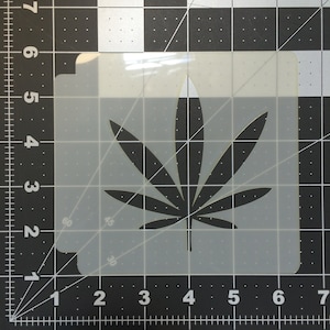 Könnte beinhalten: Eine transparente, quadratische Schablone mit einem Cannabisblatt-Design. Das Blatt ist schwarz, mit detaillierten Adern, vor einem transparenten Hintergrund. Die Schablone befindet sich auf einem schwarz-weißen Raster.