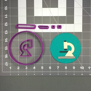 Puede incluir: Cortadores de galletas de plástico morado en forma de microscopio, círculo y rectángulo. Los cortadores están sobre un fondo de cuadrícula gris.