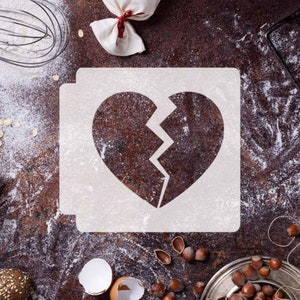 Puede incluir: Una plantilla blanca de un corazón roto sobre una superficie marrón y rústica cubierta de harina. La plantilla está rodeada de varios ingredientes para hornear, incluyendo nueces, cáscaras de huevo y un batidor.