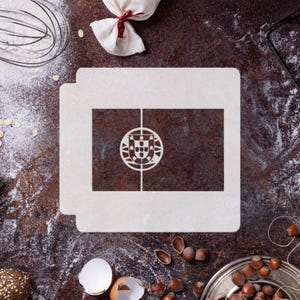 May include: A white stencil featuring the Portuguese flag design, with a rectangular shape and a detailed coat of arms in the center. The stencil is placed on a textured, dark brown surface, surrounded by baking ingredients.