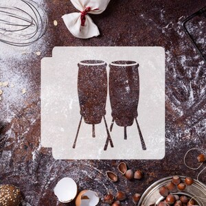 May include: A white stencil with a design of two conga drums on a brown surface with flour and other baking ingredients.