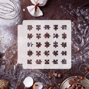 May include: A white stencil with a puzzle piece design is dusted with flour on a brown surface. The image includes a whisk, a small bag tied with a red ribbon, and scattered hazelnuts, suggesting a baking theme.