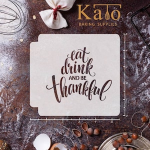 May include: A white stencil with the text "eat drink and be thankful" in a brown font. The stencil is on a brown surface with a ruler and other baking supplies.