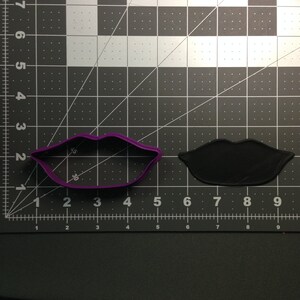 Puede incluir: Cortador de galletas de plástico morado con forma de labios. El cortador está sobre un fondo de cuadrícula blanco y negro.