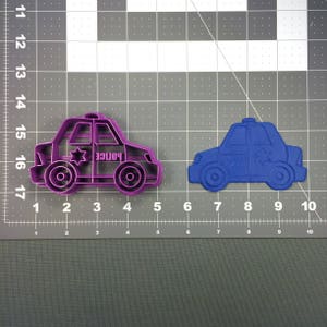 Pode incluir: Dois cortadores de biscoitos de plástico em forma de carro de polícia, um roxo e outro azul. Ambos os cortadores têm uma estrela de David e a palavra "Police" no lado.