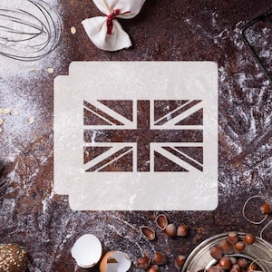 Peut inclure: Un pochoir blanc représentant le drapeau britannique sur une surface brune recouverte de farine. On aperçoit d'autres ustensiles de cuisine en arrière-plan, notamment un fouet, un sac de farine et un bol de noix.
