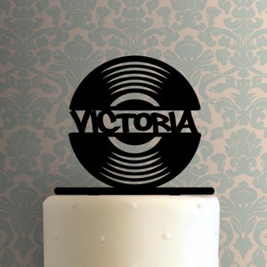 May include: Black vinyl record cake topper with the name "VICTORIA" written across the center.