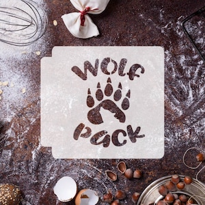 May include: A white stencil with the words "Wolf Pack" and a bear paw print. The stencil is on a brown surface with flour scattered around it.