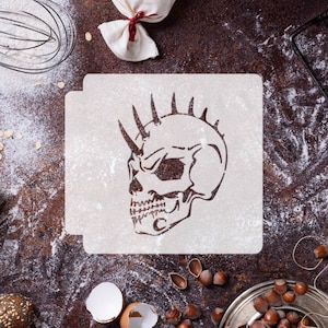 May include: White plastic stencil of a skull with spikes on its head. The stencil is on a brown surface with flour scattered around it.