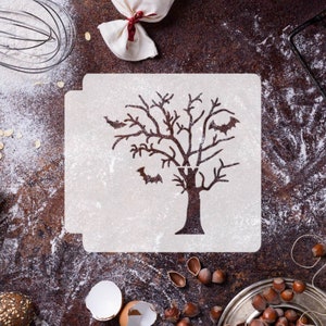 May include: White stencil with a bare tree and bats cut out. The stencil is on a brown surface with flour scattered around it.