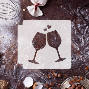 Peut inclure: Un pochoir blanc avec un motif de deux verres à vin qui trinquent avec trois petits cœurs au-dessus. Le pochoir est sur une surface brune avec de la farine éparpillée autour.