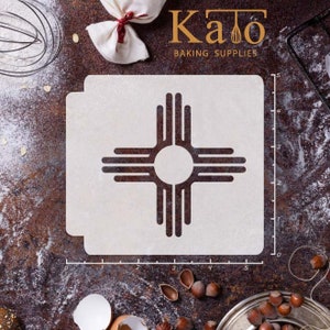 May include: A white stencil with a black outline of the Zia symbol, a traditional symbol of the Pueblo people of New Mexico. The stencil is 5 inches wide and 5 inches tall. The stencil is on a brown surface with flour and other baking supplies.