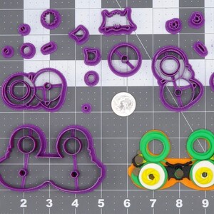 Pode incluir: Um conjunto de cortadores de biscoitos de plástico roxo em várias formas, incluindo engrenagens, um monstro e um par de olhos. Há também um cortador de biscoitos verde e amarelo em forma de óculos.