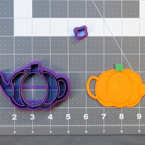 Può includere: Due stampini per biscotti in plastica a forma di teiera con corpi a forma di zucca. La teiera viola ha un manico sul lato sinistro e un beccuccio sul lato destro. La teiera arancione ha un manico sul lato destro e un beccuccio sul lato sinistro.