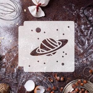 May include: White stencil with a planet and stars design on a brown surface with flour and other baking supplies.