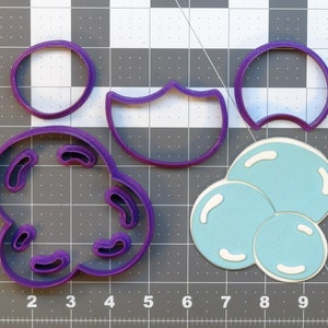 Puede incluir: Un juego de cinco cortadores de galletas de plástico morado en forma de nube, media luna, círculo y dos burbujas de diferentes tamaños.