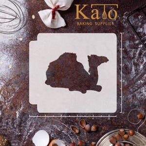 May include: A white plastic stencil featuring a camel silhouette. The stencil measures 12.7 cm wide and 10.2 cm tall. It is displayed on a brown surface with a ruler and other baking supplies.
