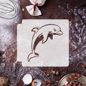 May include: A white stencil of a dolphin jumping out of the water. The stencil is on a brown surface with flour scattered around it.