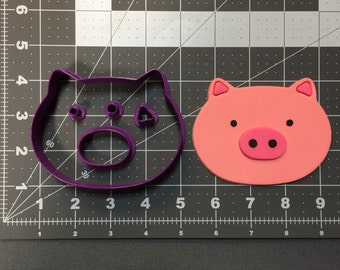 May include: A purple plastic pig cookie cutter and a pink fondant pig cookie. The cookie cutter has a detailed pig face with a snout, eyes, and ears. The fondant cookie is a simple pig face with a pink snout and black eyes.
