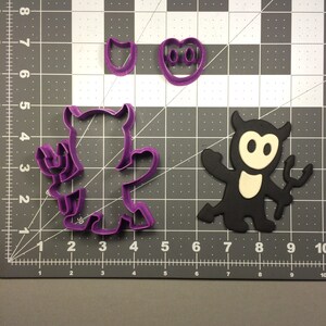 May include: Two purple plastic cookie cutters shaped like a devil with a pitchfork and a heart with two eyes. A black plastic cookie cutter shaped like a devil with a pitchfork is on the right.