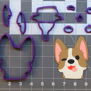 May include: Purple plastic cookie cutters in the shape of a dog, ears, tail, and a tongue. There is also a purple plastic cookie cutter in the shape of a dog's head with a winking eye and tongue sticking out.