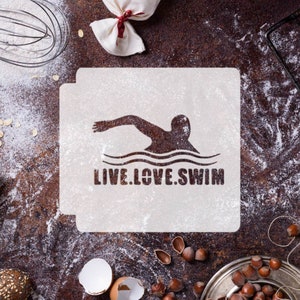 Peut inclure: Pochoir blanc avec une silhouette de nageur et le texte "LIVE.LOVE.SWIM". Le pochoir est sur une surface brune avec de la farine éparpillée autour.