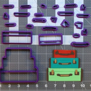 May include: Purple plastic cookie cutters in the shape of suitcases and luggage tags. The cutters are arranged on a gray gridded surface.