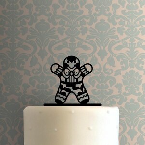 Könnte beinhalten: Ein schwarzer Lebkuchenmann-Kuchenaufsatz mit Fliege und gemusterten Details. Der Aufsatz befindet sich auf einem weißen Kuchen mit hellblauem und beigem Hintergrundmuster. Diese festliche Dekoration ist perfekt für Feiern.