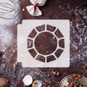 May include: A white stencil with a geometric design resembling a sun or a flower. The stencil is on a brown surface with flour scattered around it.