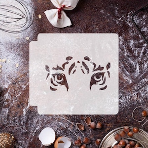 May include: White plastic stencil featuring a tiger eye design. The stencil is on a brown surface with flour scattered around it.