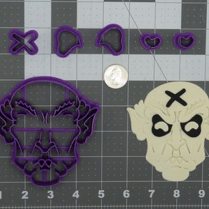 May include: Purple plastic cookie cutters in the shape of a face with a cross on the forehead, two ears, two eyes, and a mouth. There are also two heart shapes and a cross cookie cutter.