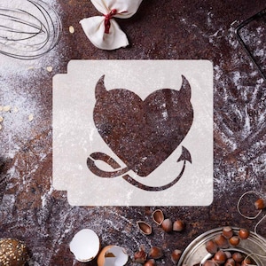 May include: White stencil featuring a heart shape with devil horns and a tail. The stencil is on a brown surface with flour and other baking supplies.