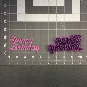 May include: Two pink plastic cookie cutters, one with the words "Happy Birthday" and the other with the words "Happy Birthday" in a different font style.