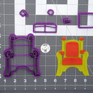 May include: Purple plastic cookie cutters in the shape of a throne chair, a back rest, and arm rests. The cutters are on a gray grid background.