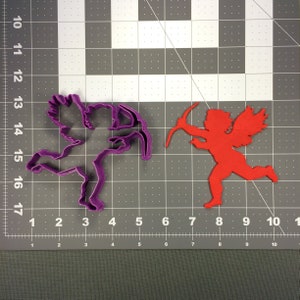 May include: Two plastic cookie cutters in the shape of a cupid holding an arrow. The cutter on the left is purple and the cutter on the right is red.