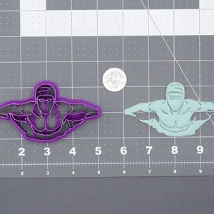 May include: Two plastic cookie cutters shaped like a swimmer in a freestyle stroke position, one is purple and the other is light green.