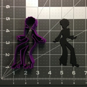Pode incluir: Cortador de biscoitos de plástico roxo em forma de uma pessoa dançando no estilo disco dos anos 70. O cortador está sobre um fundo de grade cinza.